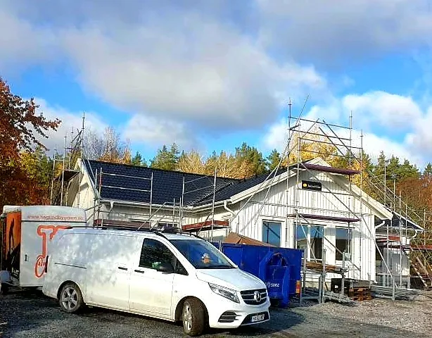 Vitt hus under byggnation med byggställning och en vit skåpbil på uppfarten
