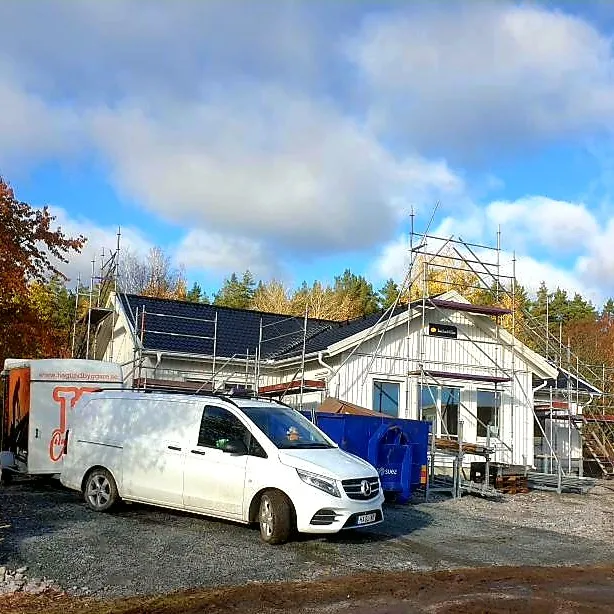 Vitt hus under byggnation med byggställning och en vit skåpbil på uppfarten