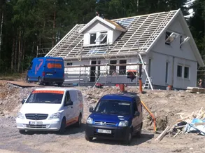 Hus under byggnation med takstolar på plats och två skåpbilar framför